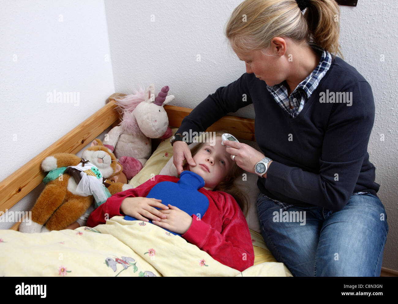 Young girl, 10 years old, is sick in bed, gets help and care from her mother. Stock Photo