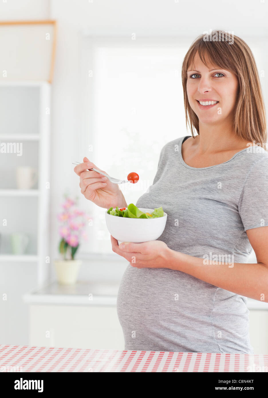 Charming pregnant woman eating a cherry tomato while standing Stock
