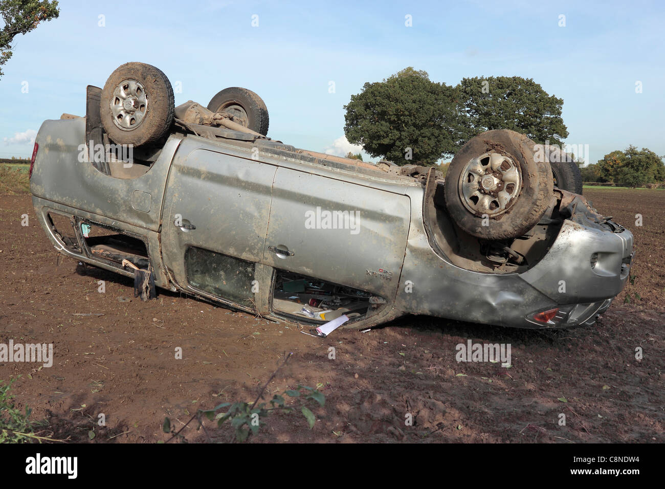 A 4 wheel drive fails to negotiate a bend on a country road and ends up on its roof in a field Stock Photo