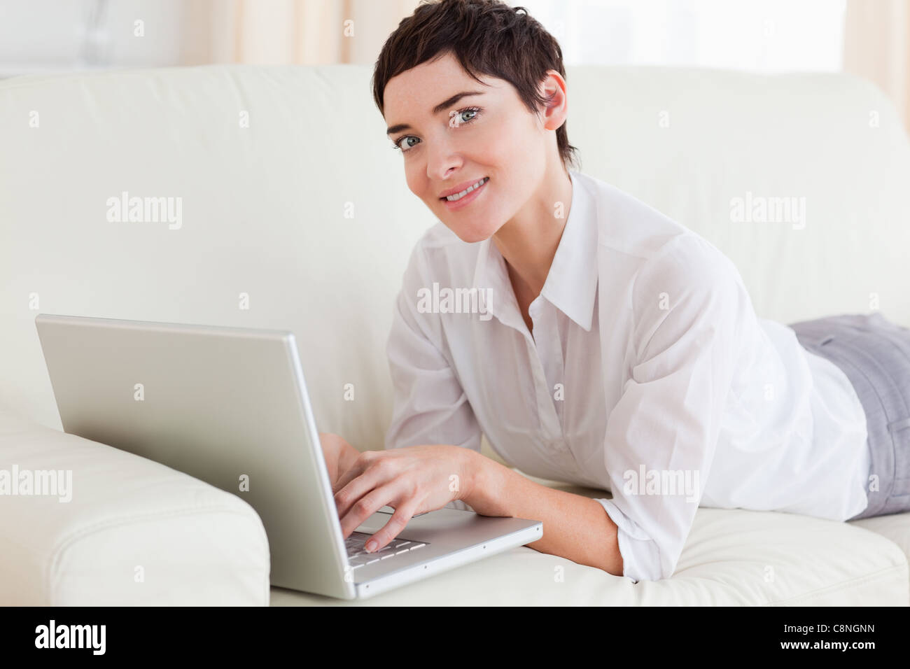 Smiling Woman lying on a sofa with a laptop Stock Photo - Alamy
