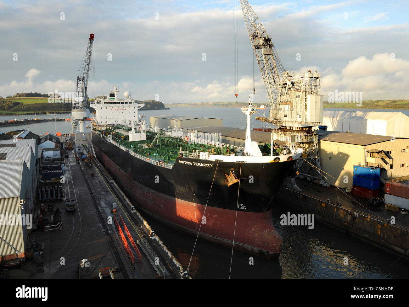 A modern supertanker at rest in a dock. Good view of bows and upper deck from a high angle. With dockside crane and buildingbasi Stock Photo