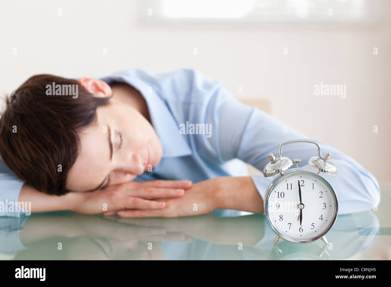Sleeping brunette woman with her head on the desk next to an alarmclock Stock Photo