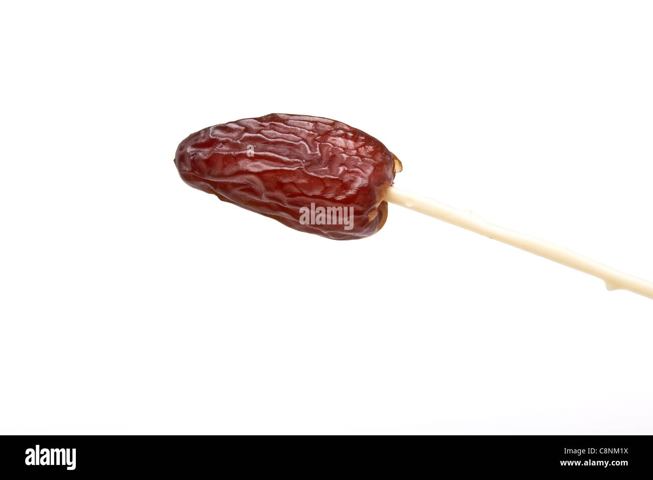 Single dried date fruit on plastic skewer used for eating them. Stock Photo
