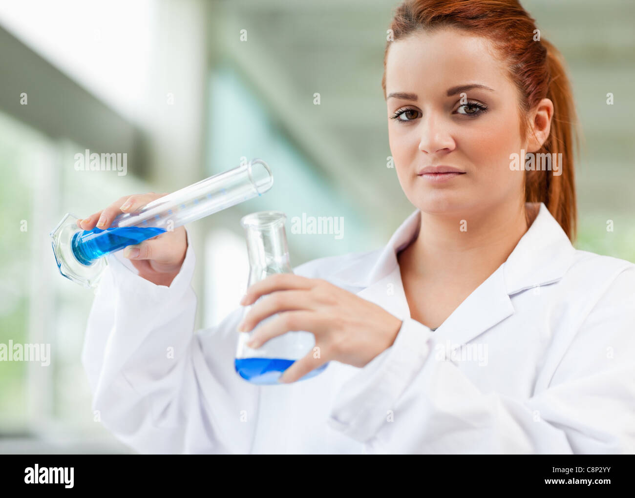 Cute scientist pouring blue liquid in an Erlenmeyer flask Stock Photo