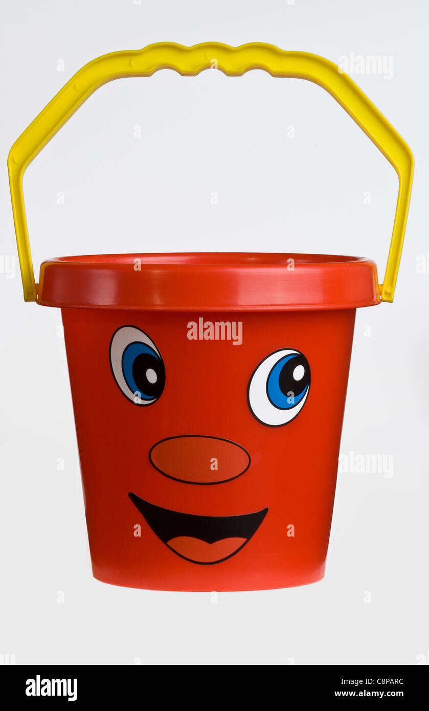 A bright red plastic child's bucket with a yellow handle and a smiley face. Stock Photo