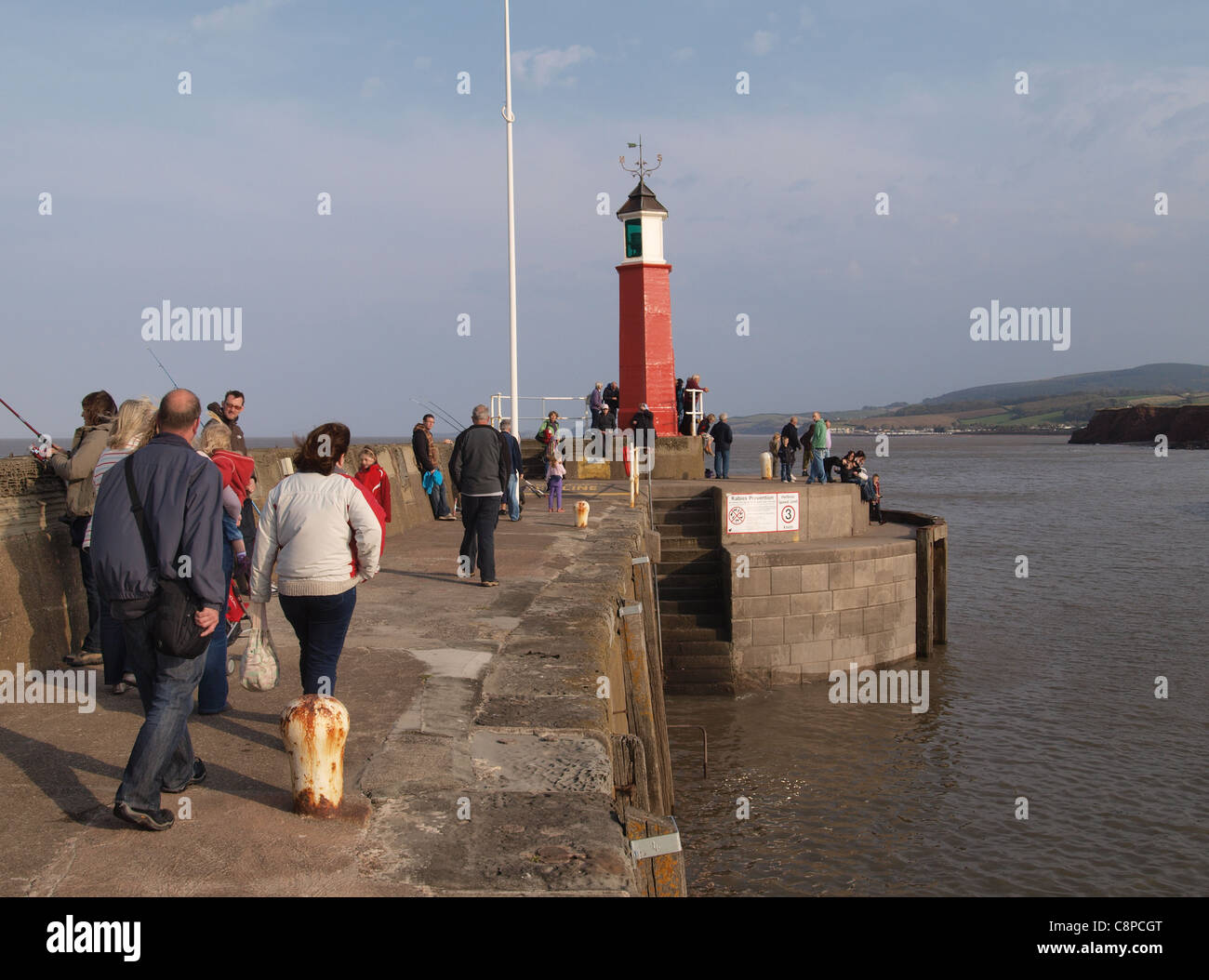 People walking and fishing along harbour wall near lighthouse. Watchet. Somerset. Stock Photo