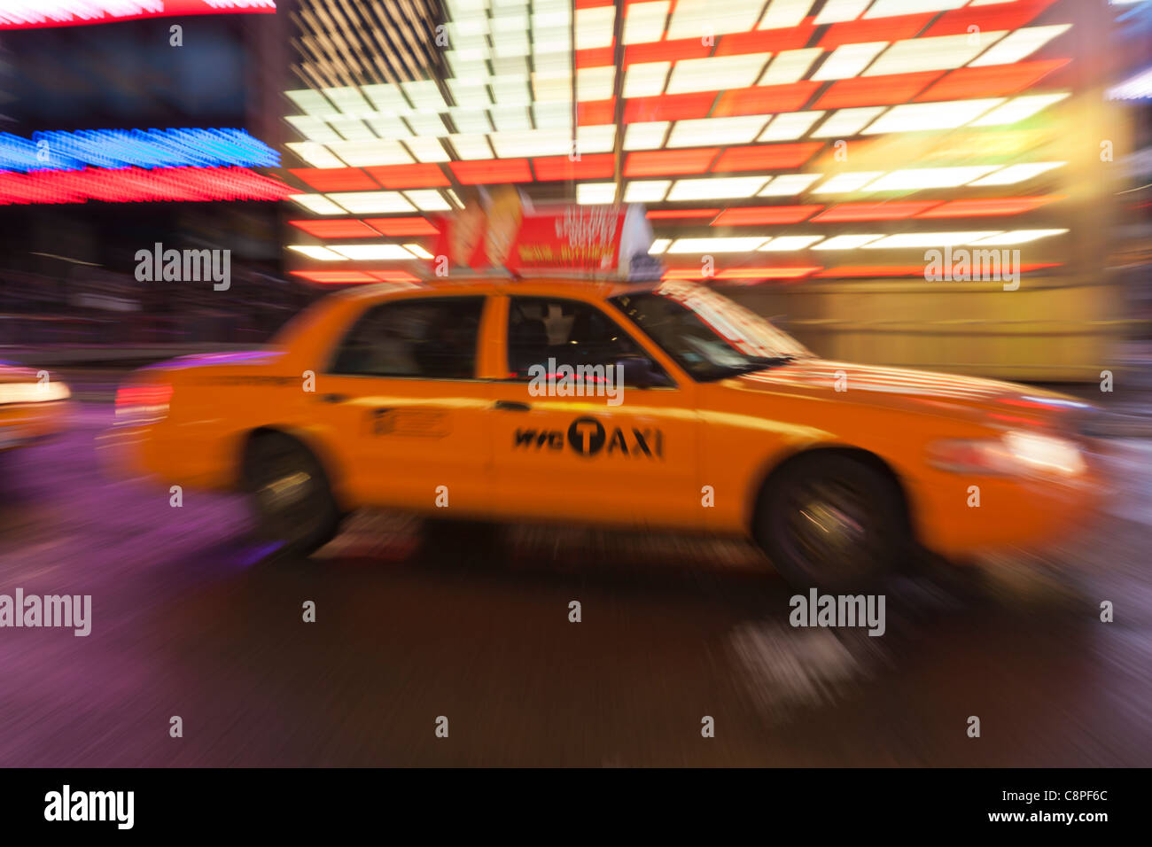 A yellow taxi cab is a blur as it rushes through the lights of Times Square at night in New York City. Stock Photo
