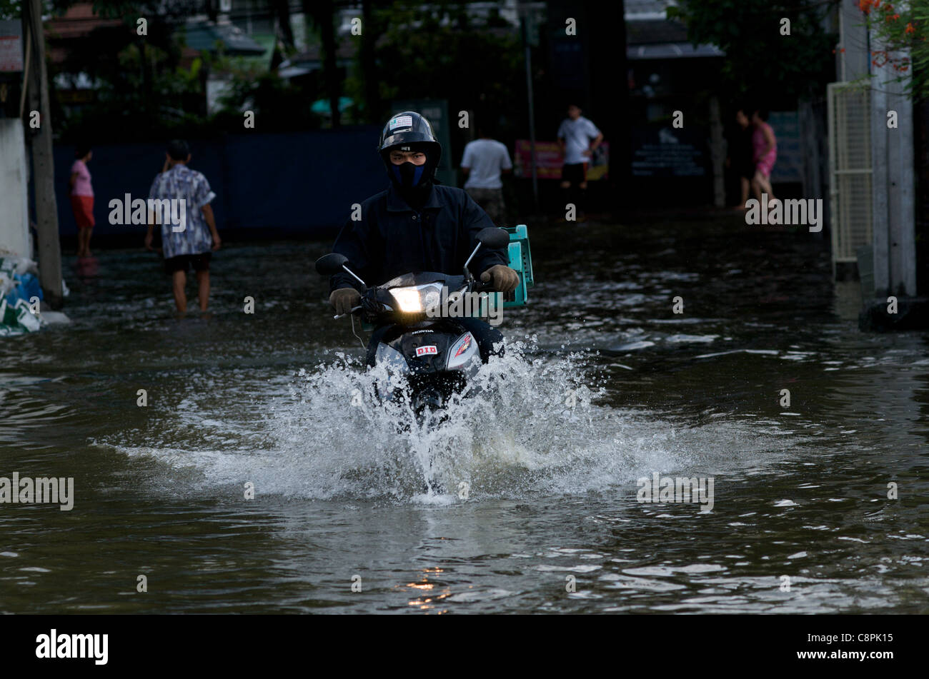 Bangkok resident drives motorcycle through flood water from the overflowing Phra Khanong Canal,  Sukhumvit Road, soi 50, Bangkok, Thailand on October 30th, 2011. Thailand is experiencing its worst flooding in more than 50 years. credit: Kraig Lieb Stock Photo