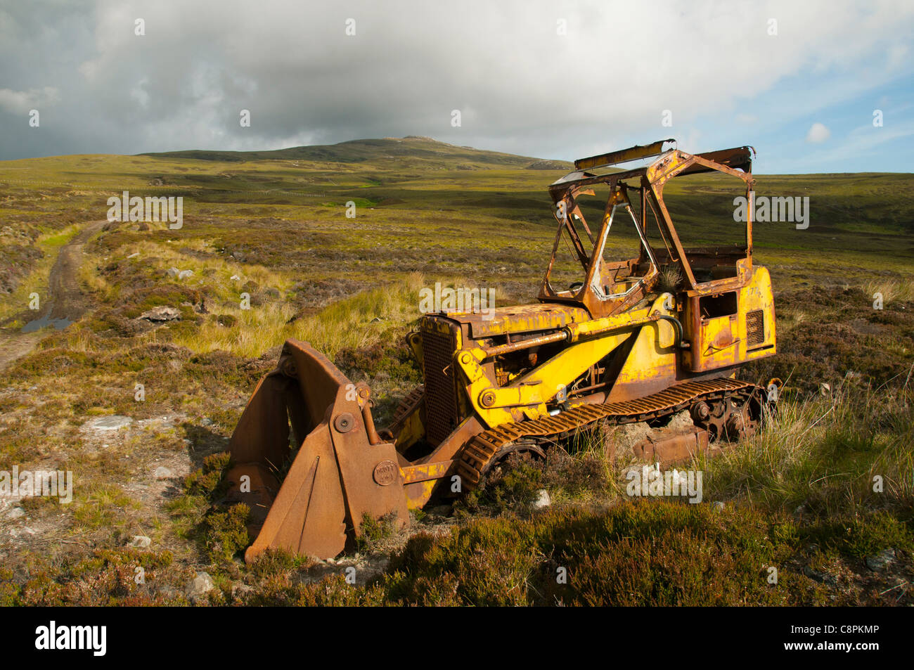 Abandoned rusting bulldozer on the slopes of Ben Hutig, Sutherland, Scotland, UK.  Ben Hutig summit is in the background. Stock Photo