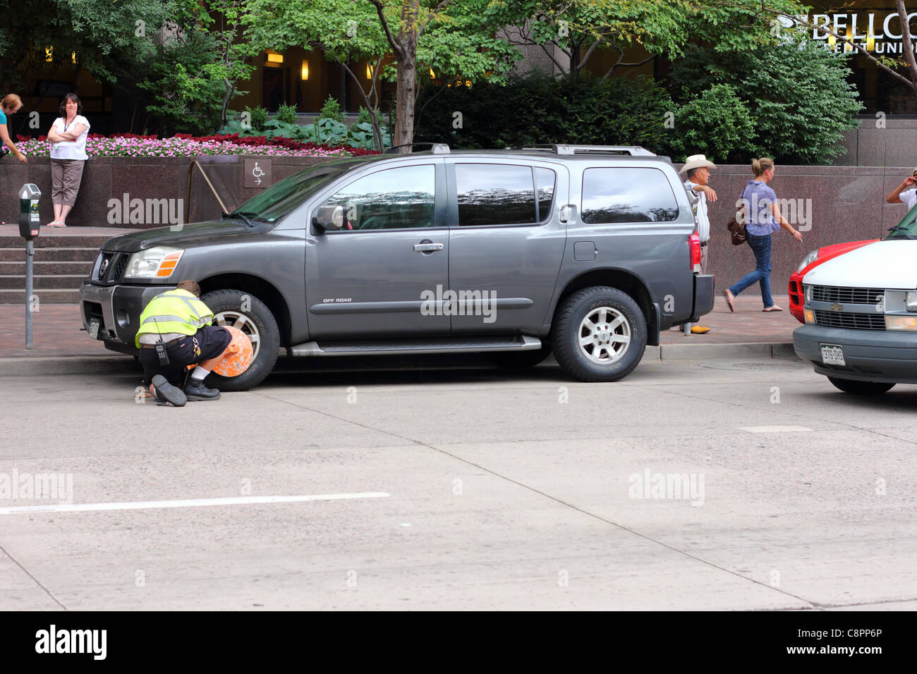 A Denver city employee applies a boot to a car for unpaid parking tickets Stock Photo