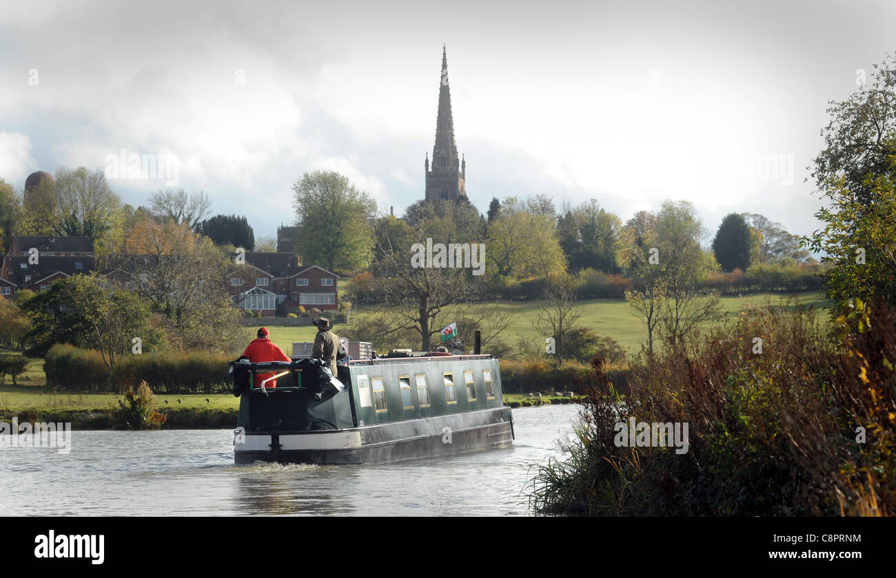 NARROWBOAT BARGE ON CANAL WITH COUNTRYSIDE AND CHURCH SPIRE RE BOATING HOLIDAYS RETIREMENT RELAXING LIFESTYLE ETC UK Stock Photo