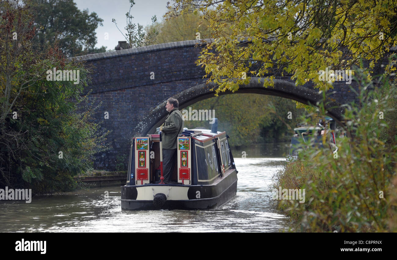 MAN ON NARROWBOAT BARGE ON CANAL WITH BRIDGE RE BOAT HOLIDAYS RELAXING RETIREMENT LIFESTYLE WATERWAYS ETC UK Stock Photo