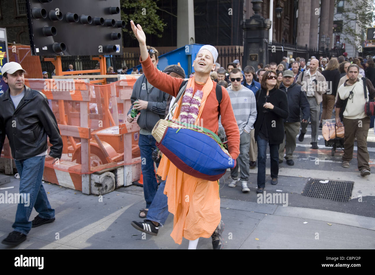 Joyful Hari Krishna devotee walks and plays his drum on Broadway in the financial district in NYC Stock Photo