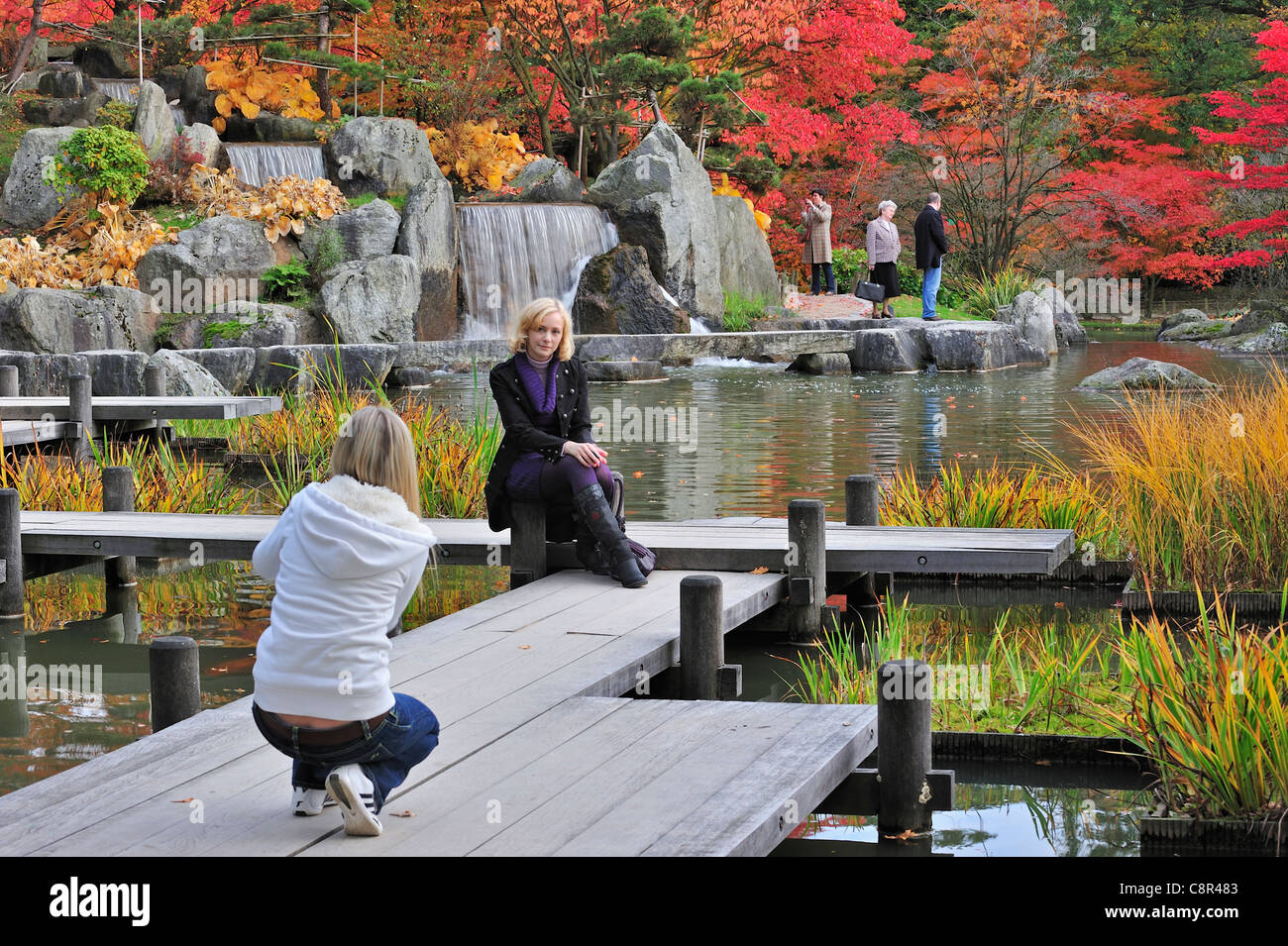 Tourist posing for camera on wooden gangway in Japanese garden with tree foliage in red autumn colours in Hasselt, Belgium Stock Photo