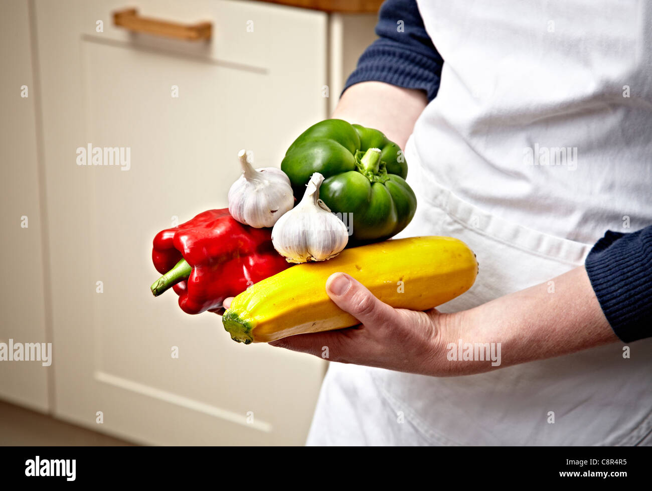Chef holding various vegetables in hands in modern kitchen setting. Chef is wearing white apron. Stock Photo
