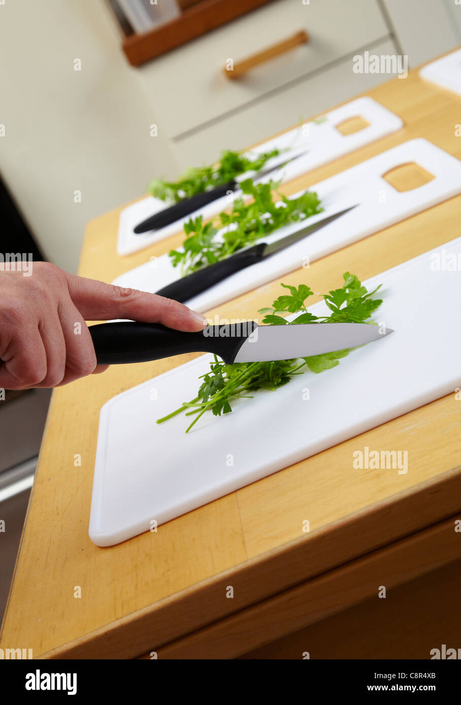 Green herbs on chopping board with kitchen knife. Ready for chopping in cookery class. Hand holding knife demonstrates chopping Stock Photo