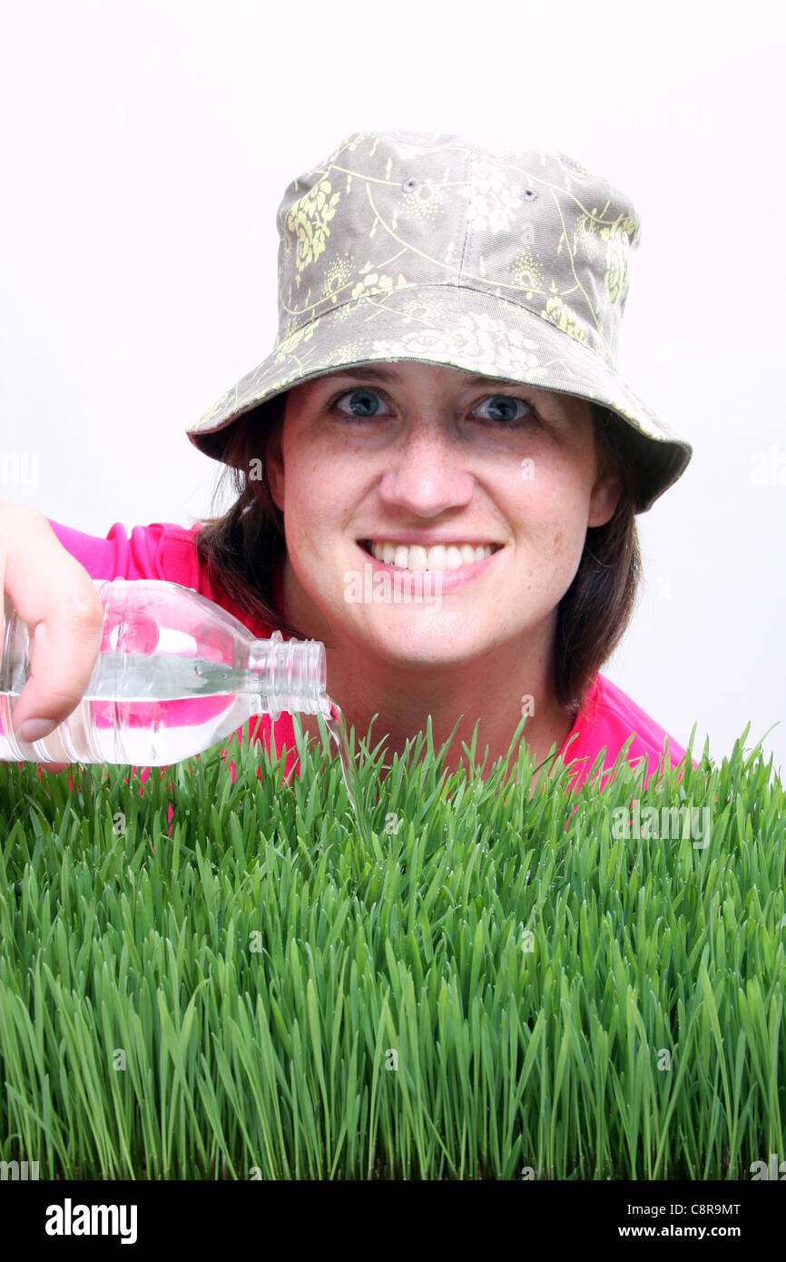 A young woman pouring water on grass from a bottle focus on water Stock