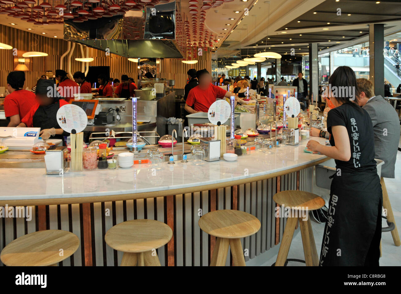 People & YO Sushi restaurant business food in bowls on a rotating  conveyor belt display Westfield shopping Centre at Stratford City London England UK Stock Photo