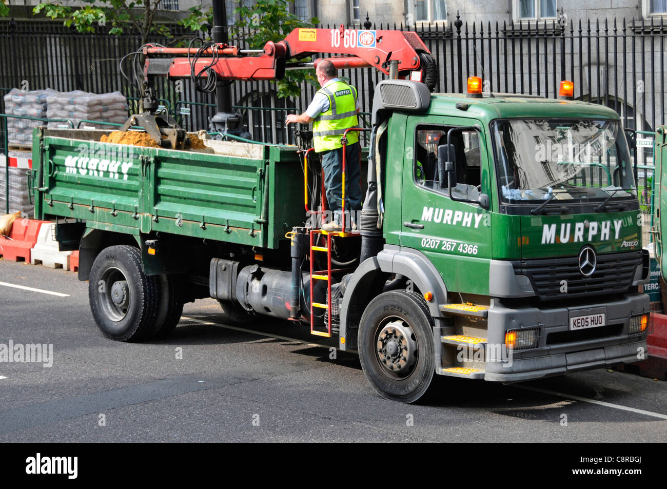Tipper truck driver operating controls of grab crane bucket loader on back of Murphy dual purpose Mercedes lorry beside road works London England UK Stock Photo