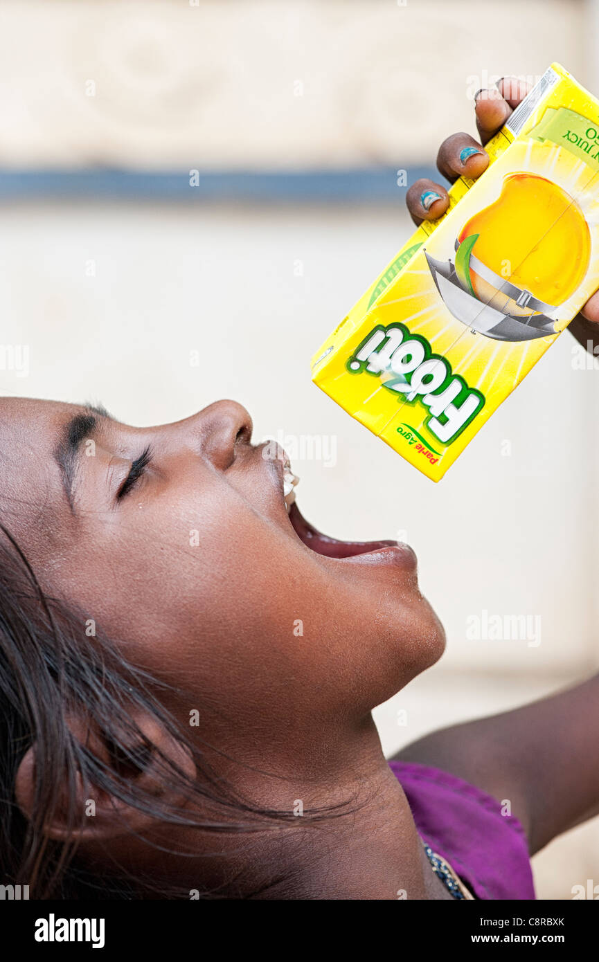 Young poor lower caste Indian street girl trying to get the last drops out of a carton of fruit juice. India Stock Photo