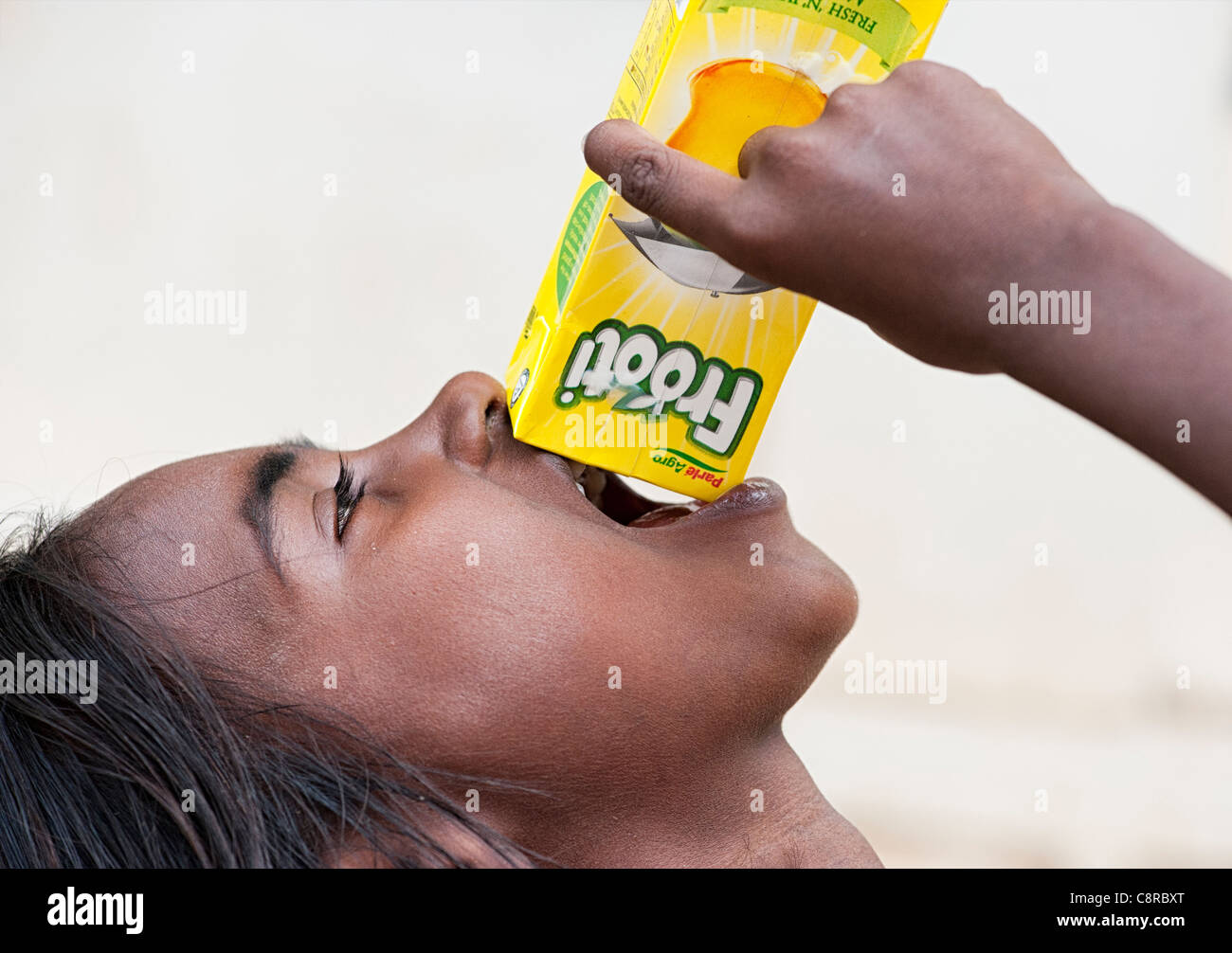 Young poor lower caste Indian street girl trying to get the last drops out of a carton of fruit juice. India Stock Photo