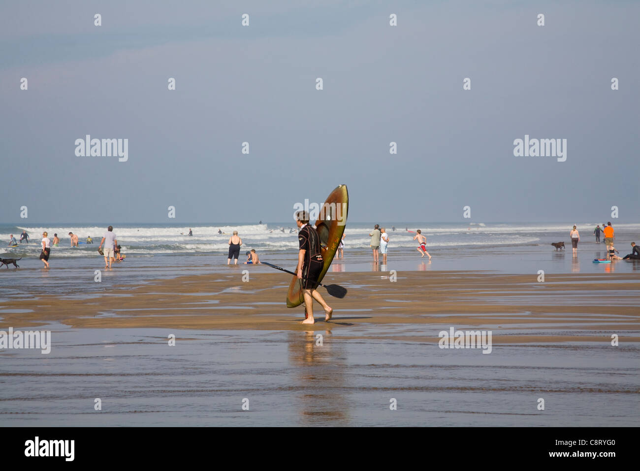 Bude Cornwall England Young man in wetsuit carrying kayak into surf