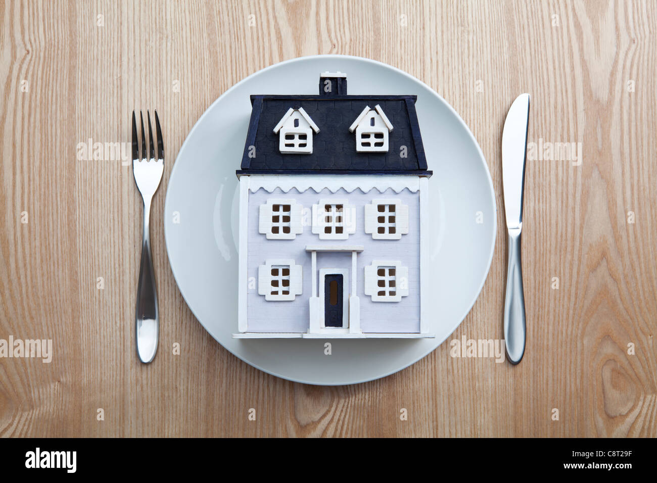 Top view of model house placed in plate with fork and knife on table Stock Photo