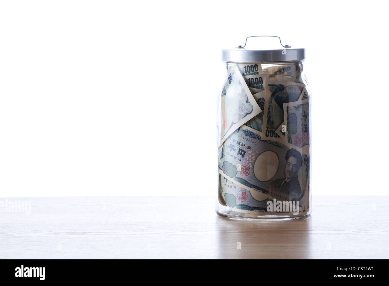 One Thousand Yen Notes inside of glass jar against white background Stock Photo