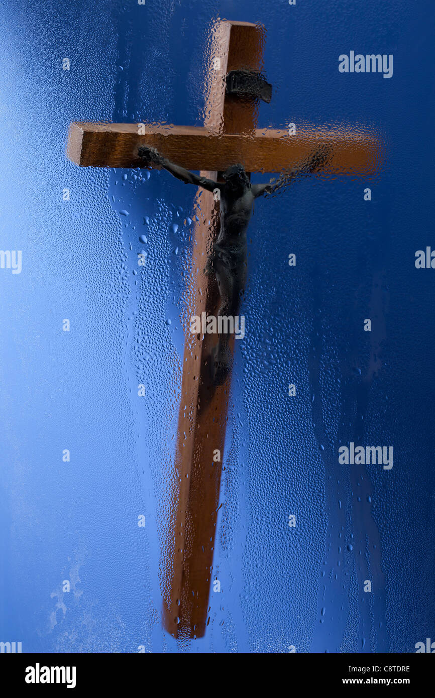 Blurred crucifix shot through glass against blue background Stock Photo