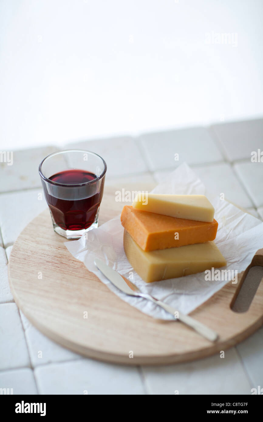 Close-up of glass of wine and slice of cheese placed on cutting board Stock Photo