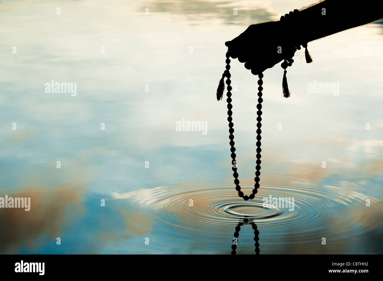 Hand holding Indian Rudraksha / Japa Mala prayer beads over rippling water . Silhouette Stock Photo