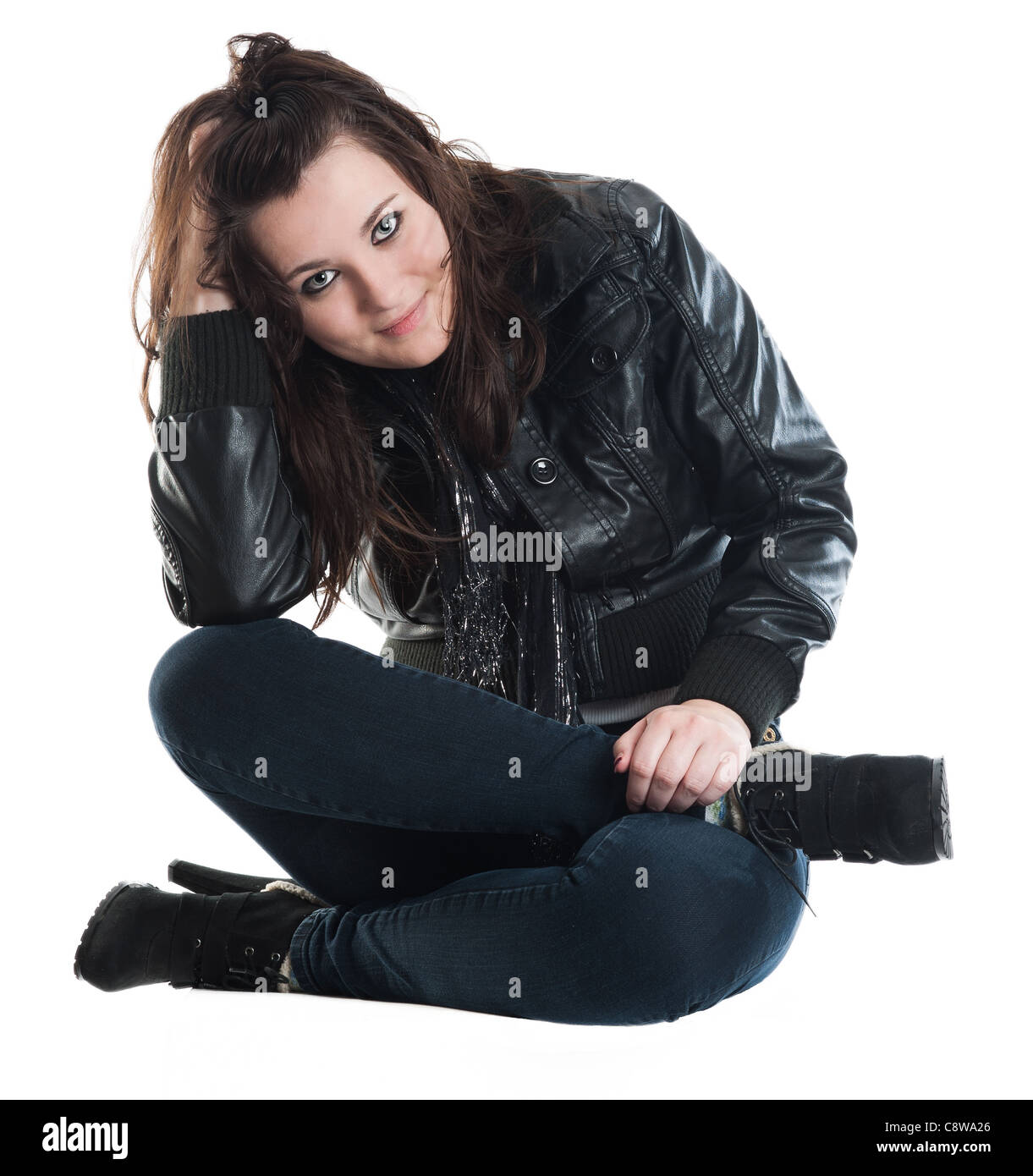 Young woman in leather jacket and blue jeans, sitting cross-legged on the floor. Stock Photo