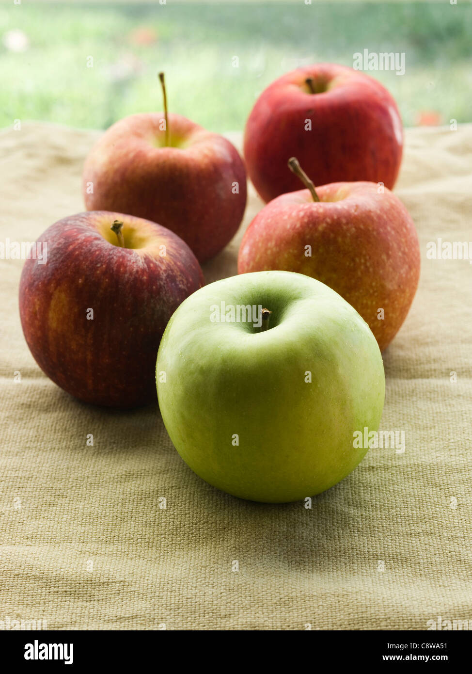One green apple and four red apples Stock Photo