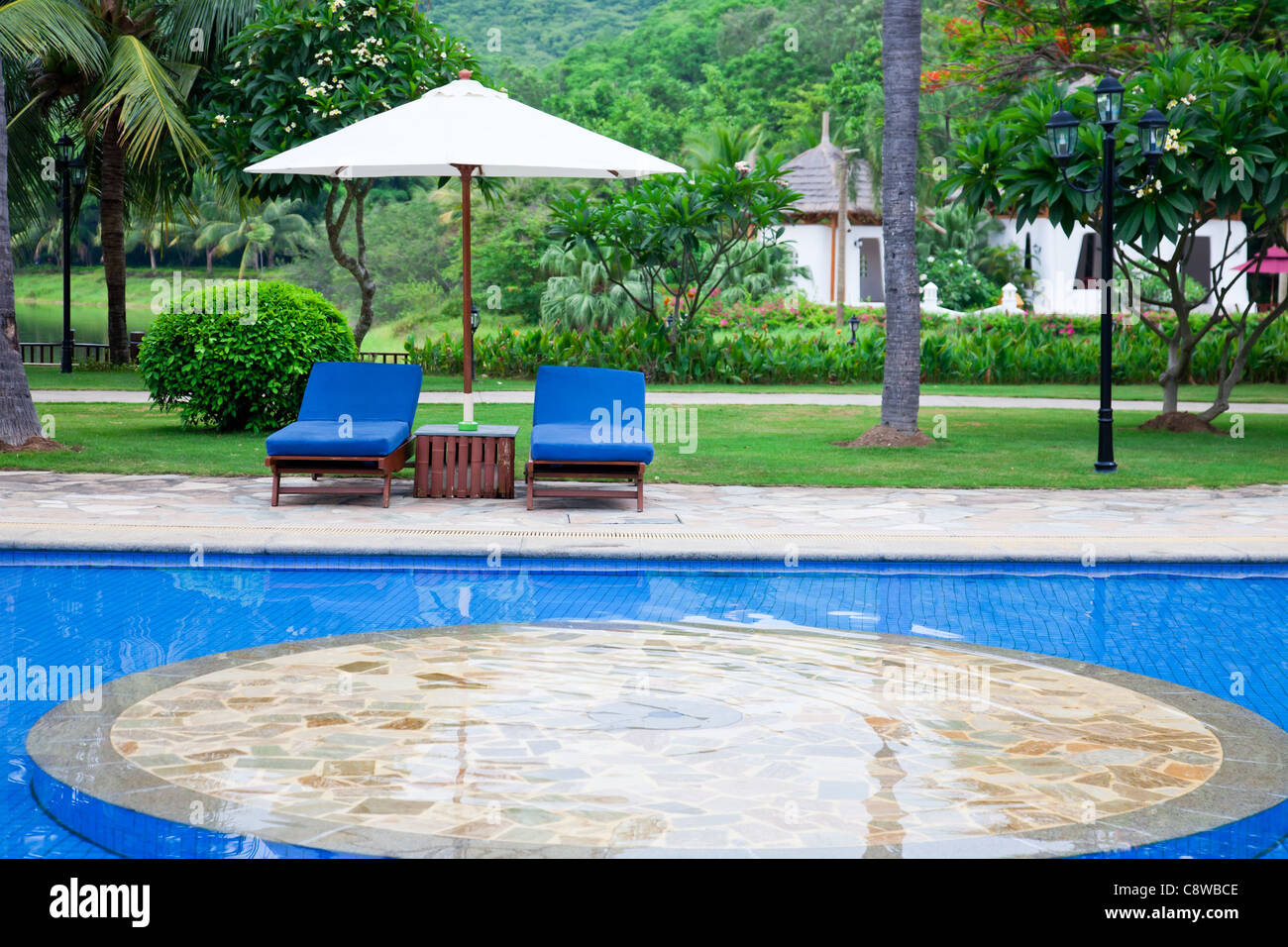 Recliners and umbrella at the poolside of a tropical garden. Stock Photo