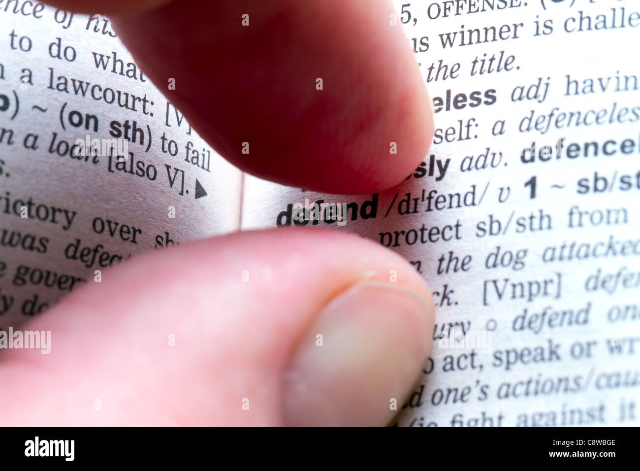 Fingers highlighting word Defend in dictionary by framing it. Stock Photo