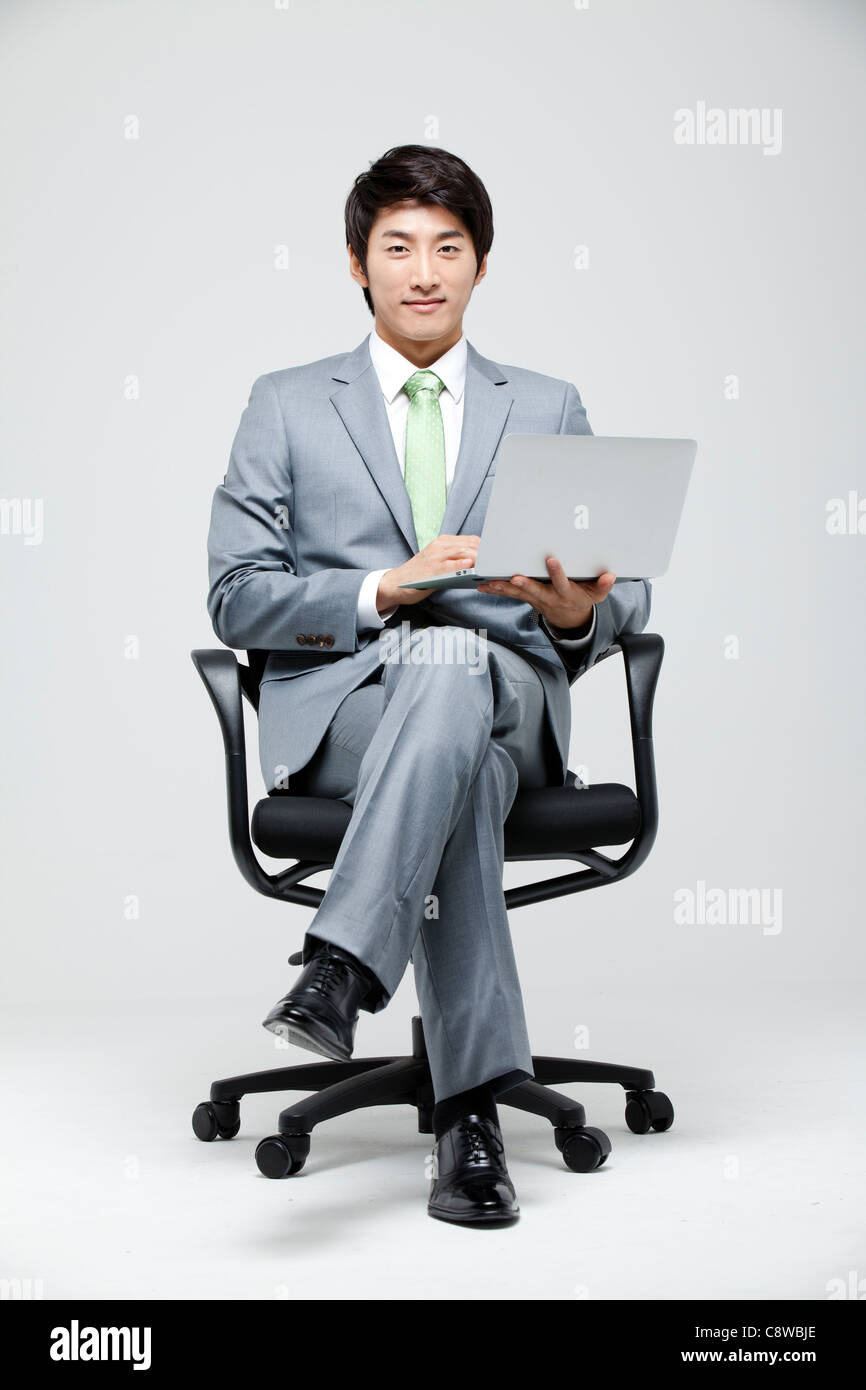 Asian Businessman Sitting On Chair With Leg Crossed Holding Laptop In ...