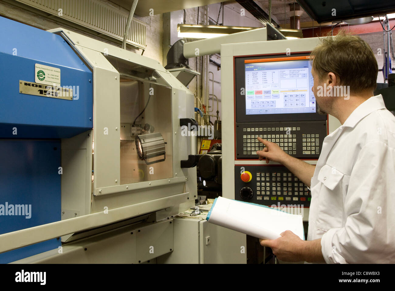 engineer programs parameters into a CNC gear-cutting lathe in workshop Stock Photo