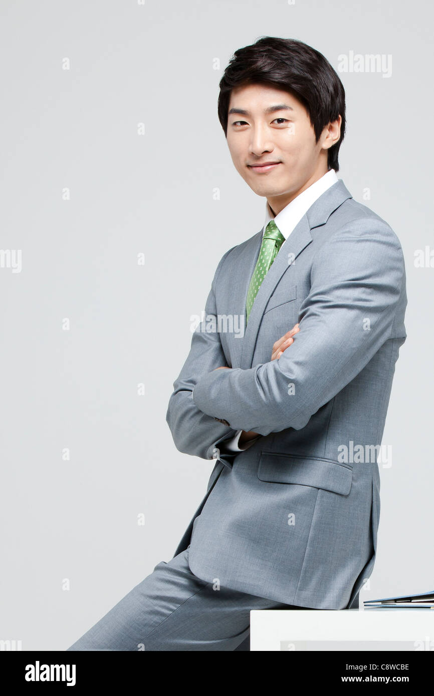 Portrait Of Smiling Asian Businessman Sitting On Desk With Arm Crossed ...