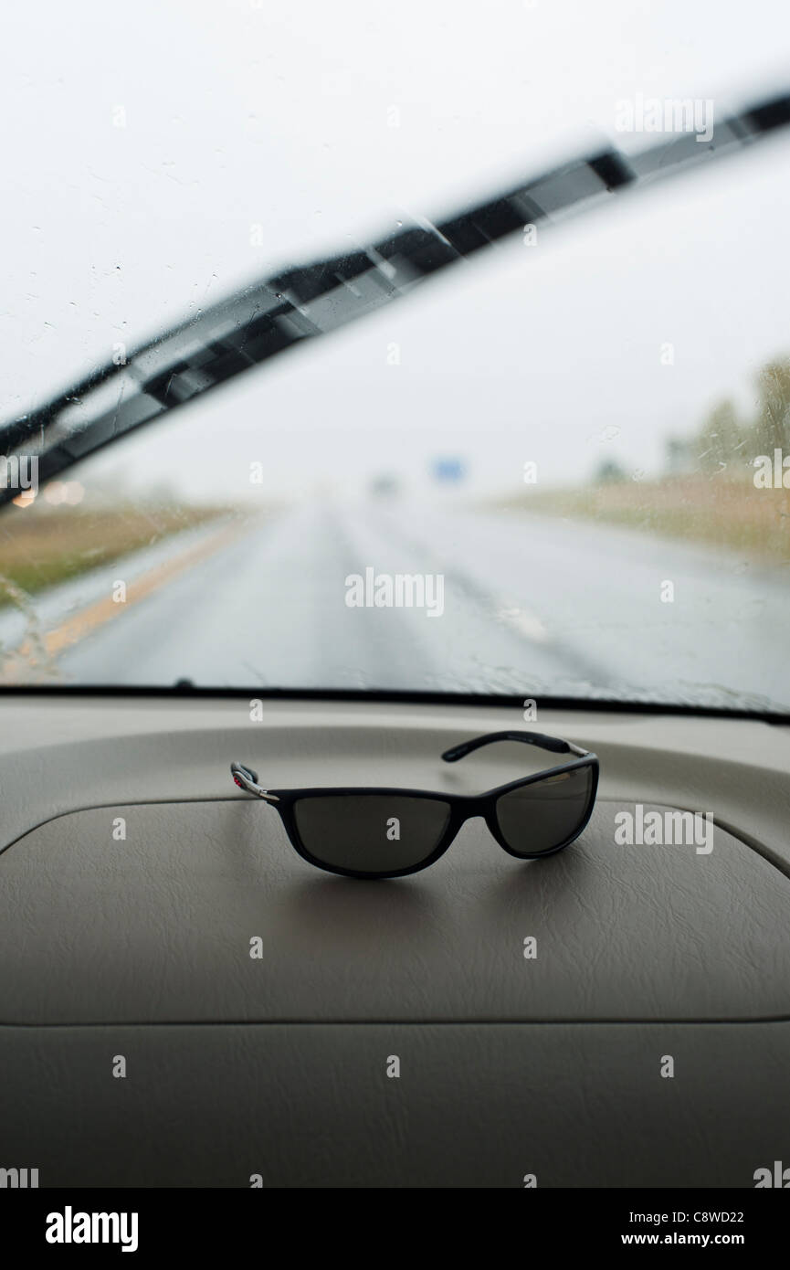 Sunglasses on a car dashboard with windshield wiper in action on a rainy day Stock Photo