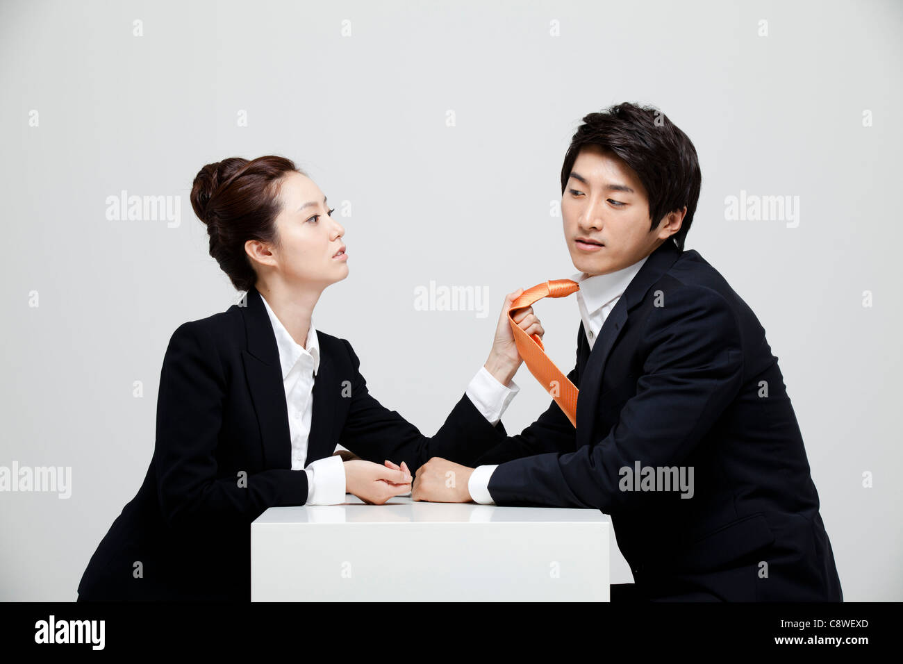 Asian Businesswoman Holding Tie Of Businessman At Desk Facing Each Other Stock Photo