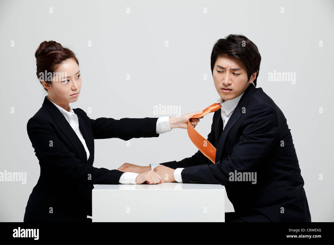 Asian Businesswoman Holding Tie Of Businessman At Desk Facing Each Other Stock Photo