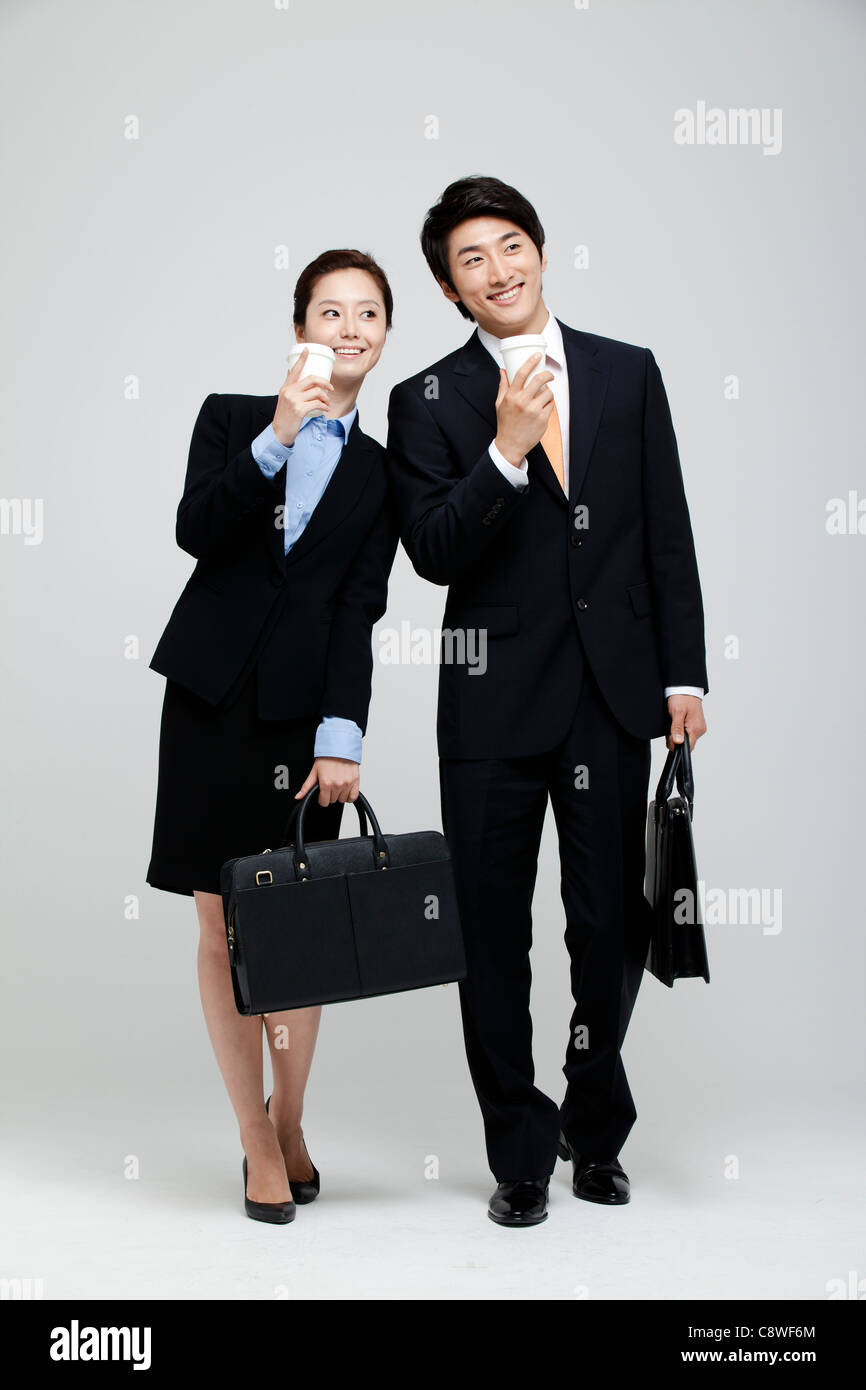 Asian Businesswoman And Businessman Holding Takeaway Coffee And Suitcase In Hand Stock Photo