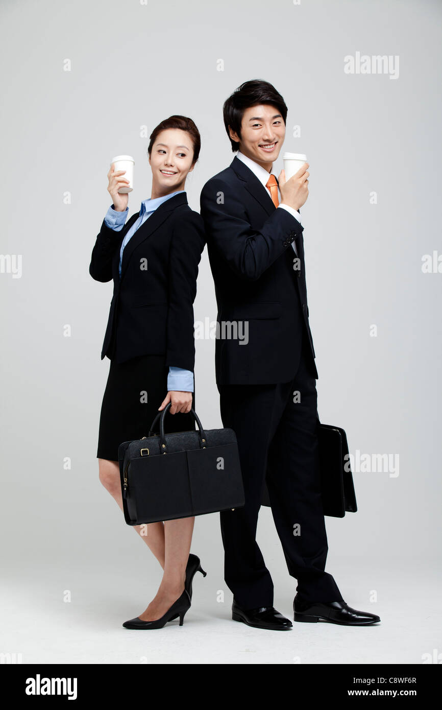 Asian Businesswoman And Businessman Holding Takeaway Coffee And Suitcase In Hand Stock Photo