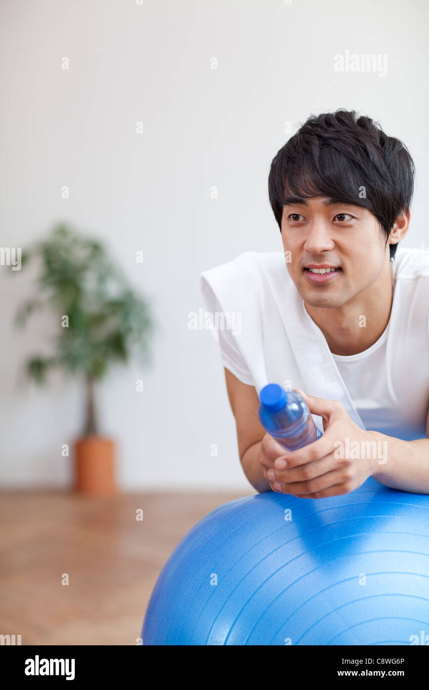 Asian Man Leaning On Pilates Ball Holding Water Bottle Stock Photo
