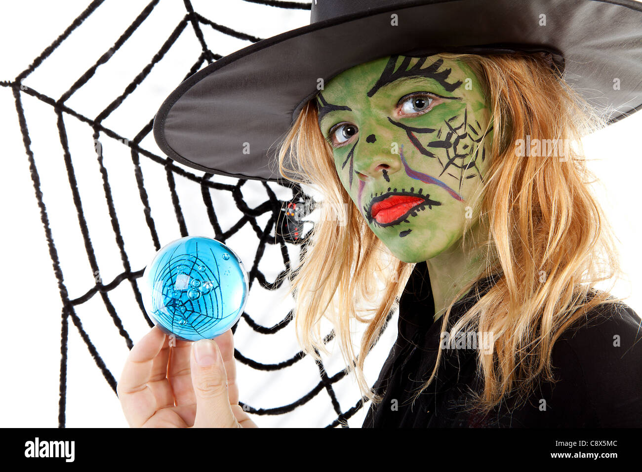 Portrait of green Halloween witch girl in closeup holding big blue marble Stock Photo