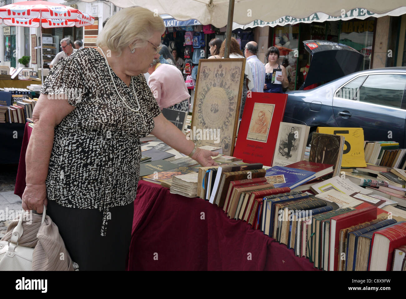 A woman inspecting books at a flea market, held on the last Saturday of the month, in Praça do Comércio, Coimbra, Portugal. Stock Photo