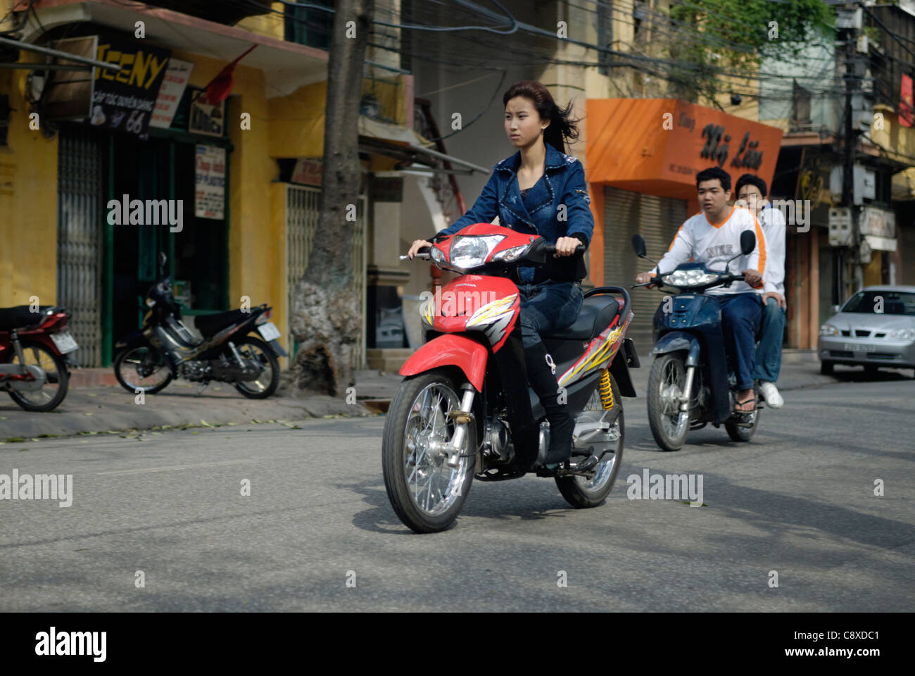 Asia, Vietnam, Hanoi. Hanoi old quarter. Young vietnamese woman riding a small motorbike through Hanoi.... Stock Photo