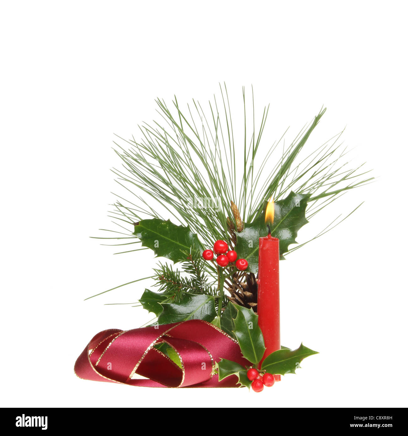 Christmas decoration of seasonal foliage, ribbon and a burning candle isolated against white Stock Photo