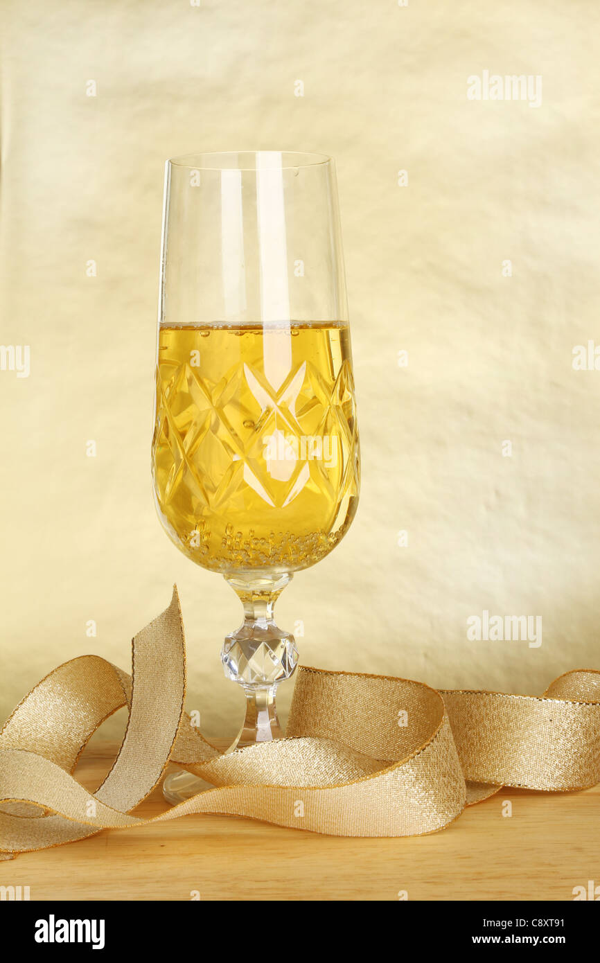 Glass of champagne and a gold ribbon against a gold background Stock Photo