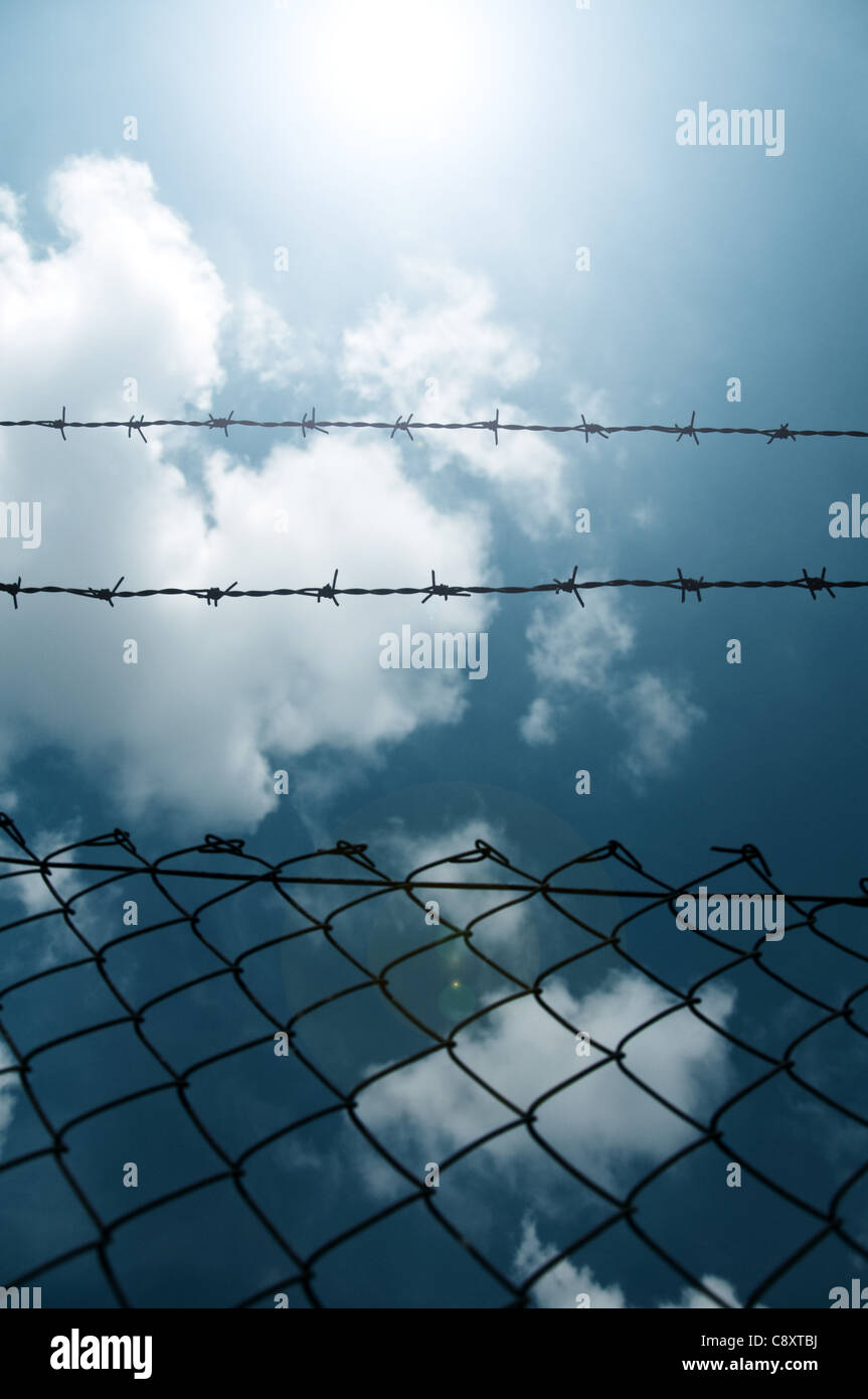 Barbed wire fence against a blue sky with clouds Stock Photo